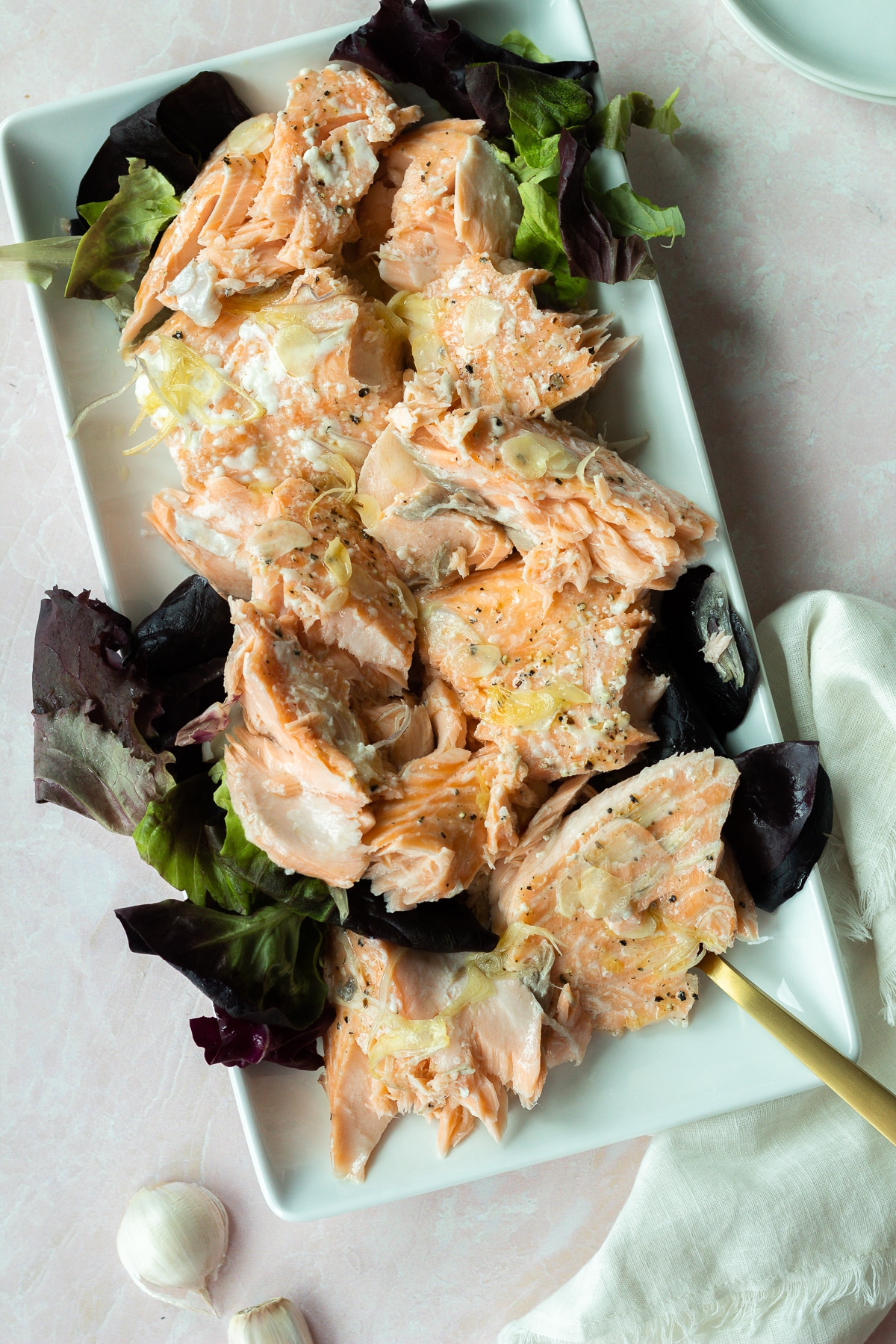 Salmon on white serving platter with gold silverware and white linen napkin.