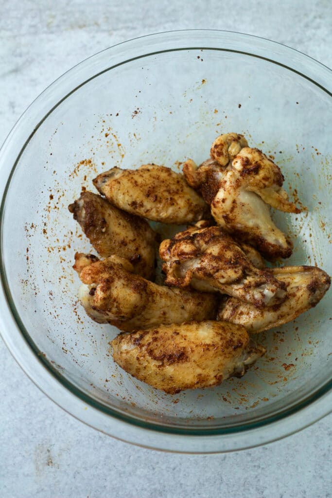 Chicken wings tossed with seasoning in bowl.