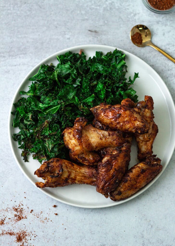Cooked air fryer frozen chicken wings on plate with side of kale.