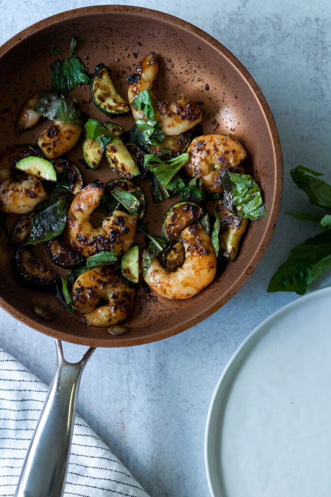 Shrimp and basil stir fry in pan with empty plate.