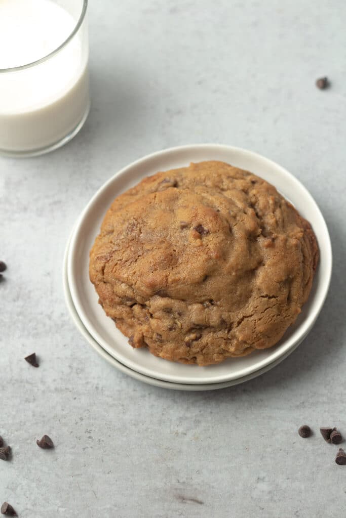 Giant chocolate chip cookie on plate with glass of milk.