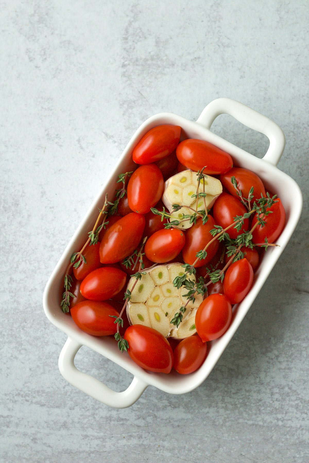 Cherry tomatoes, garlic and thyme in baking dish.
