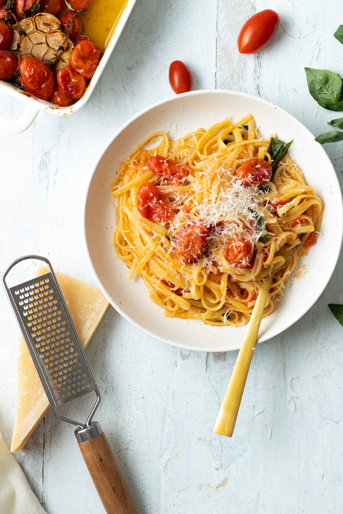 Bowl of pasta with tomato confit and parmesan on side.