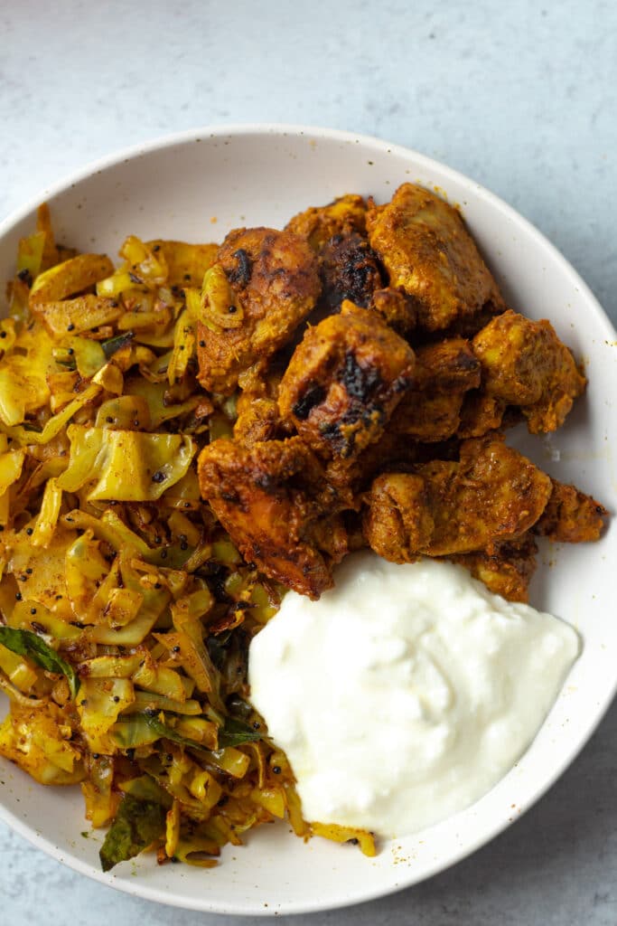 Indian spiced broiled chicken on plate with cabbage.