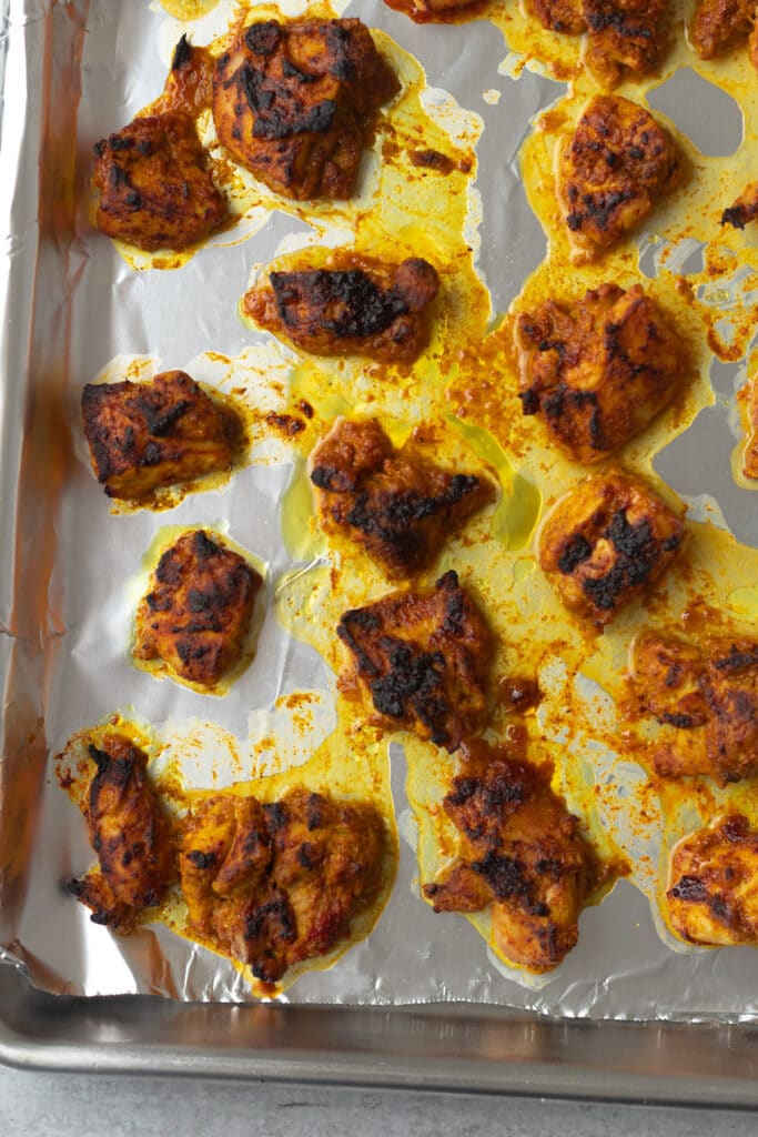Broiled indian spiced chicken chunks on baking sheet.