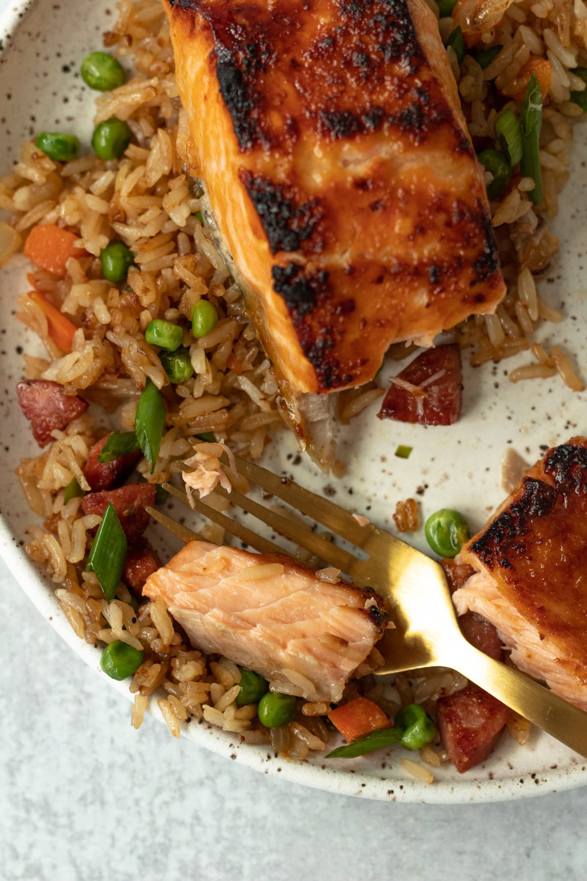 Bite of salmon and rice on fork on plate.