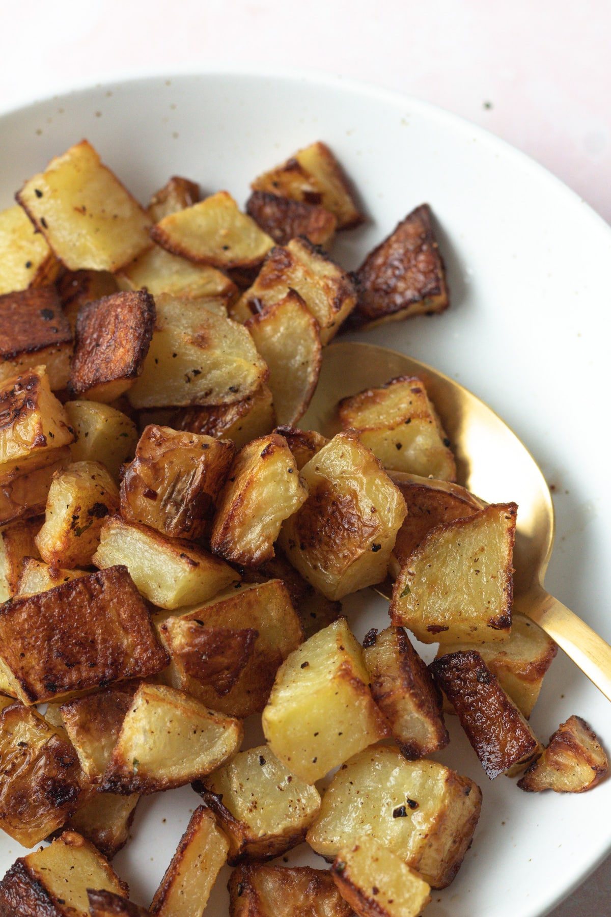 Close up shot of crispy roasted potatoes in plate with spoon.