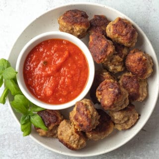 Plate of meatballs with marinara sauce on side.