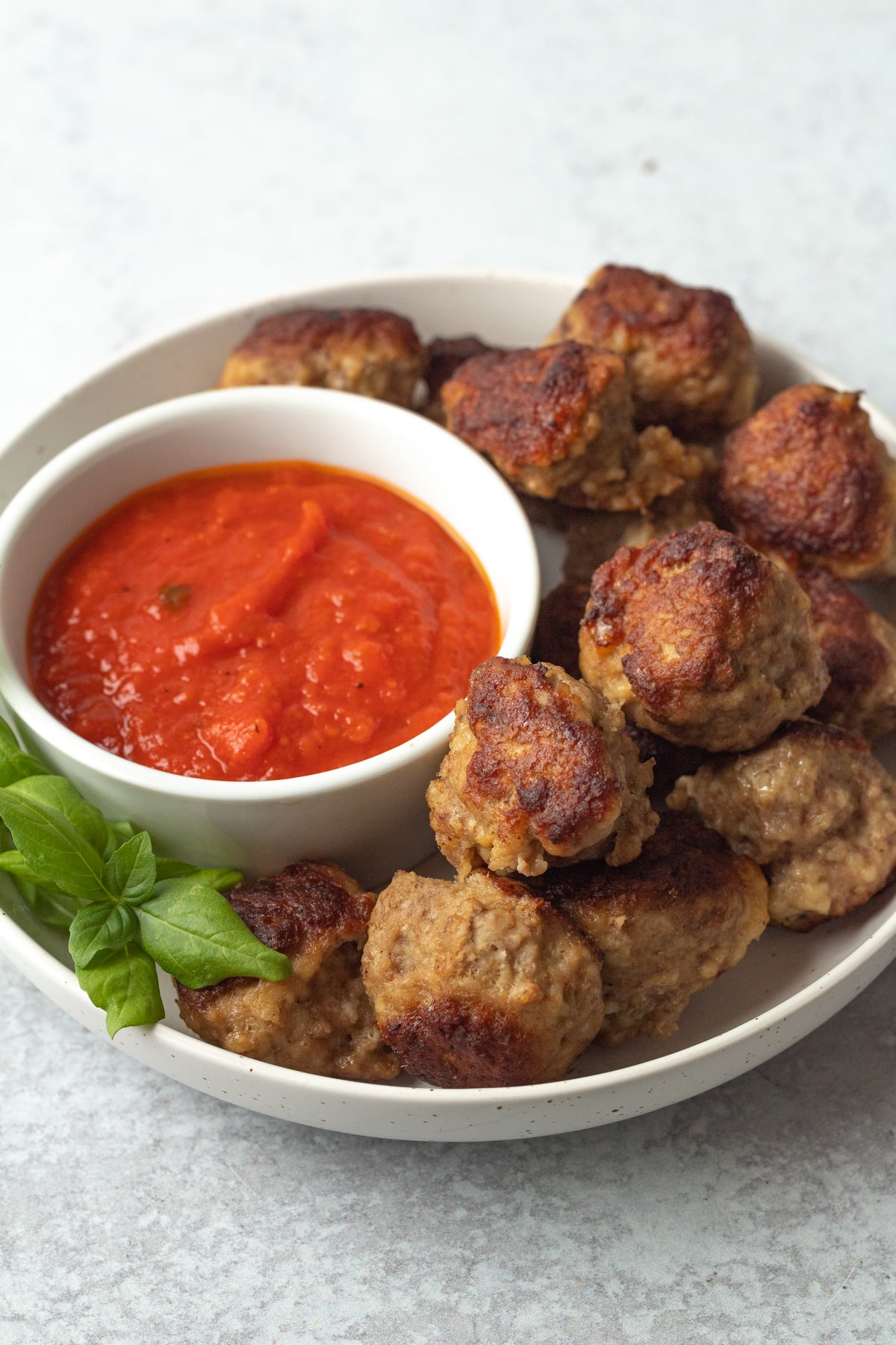 Bowl of marinara sauce with meatballs on plate.