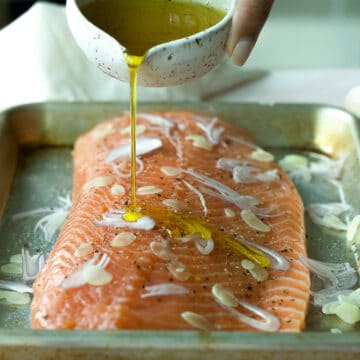 Salmon on sheet pan with shallots and olive oil poured on top.