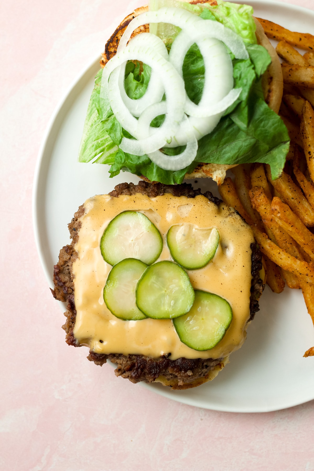 Refrigerator dill pickles on top of burger patty on plate.