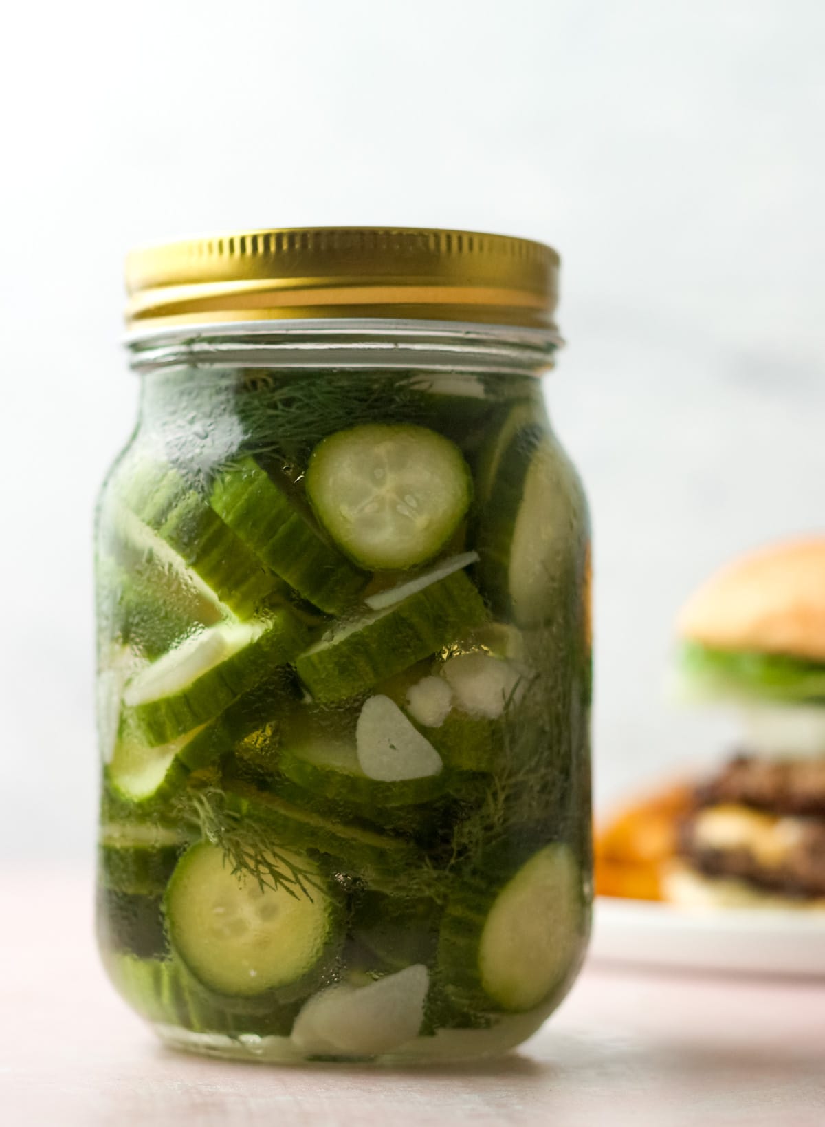 One pint jar with pickles, with burger on plate behind.