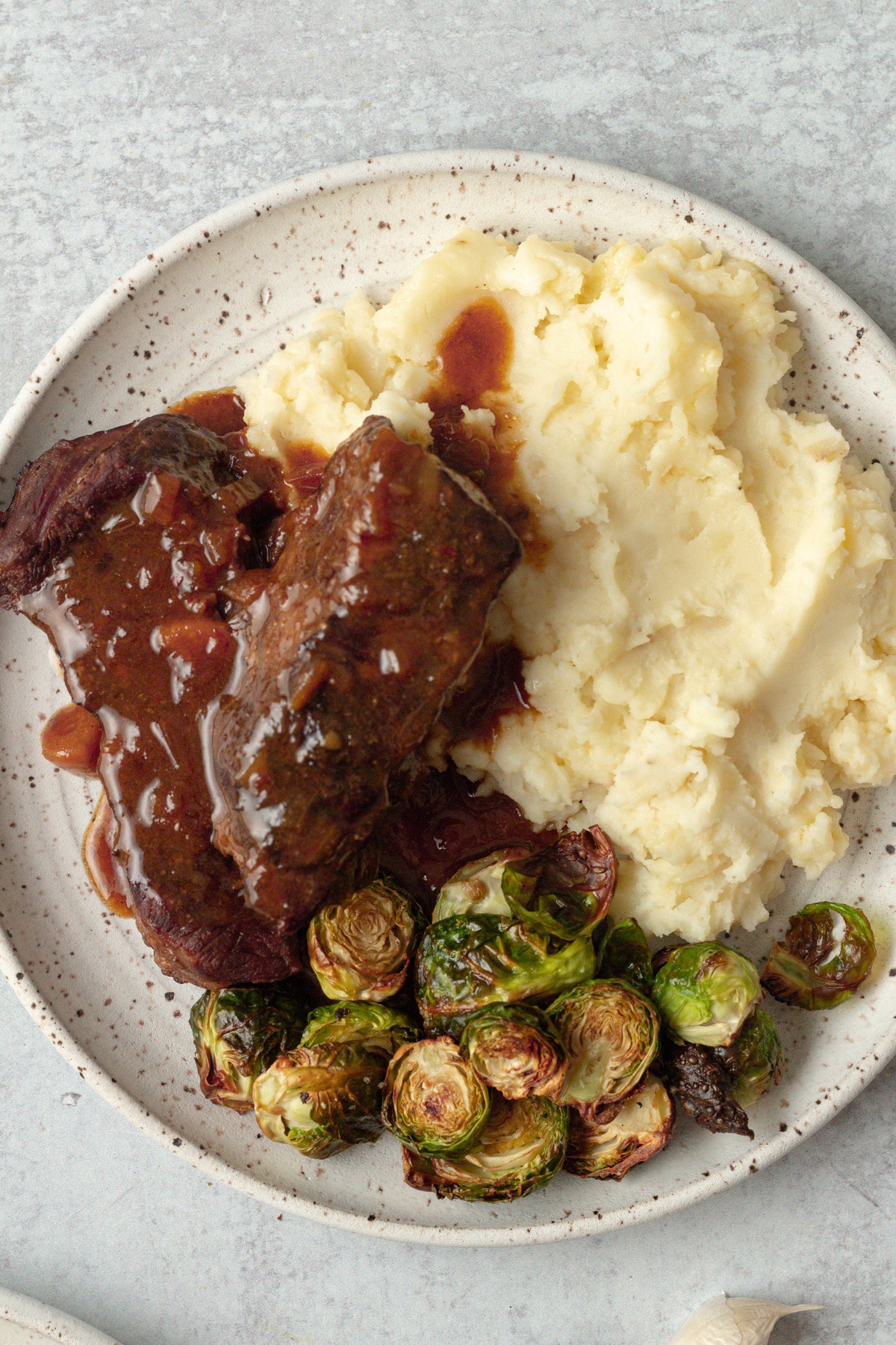 Short ribs with gravy on top of mashed potatoes on plate.