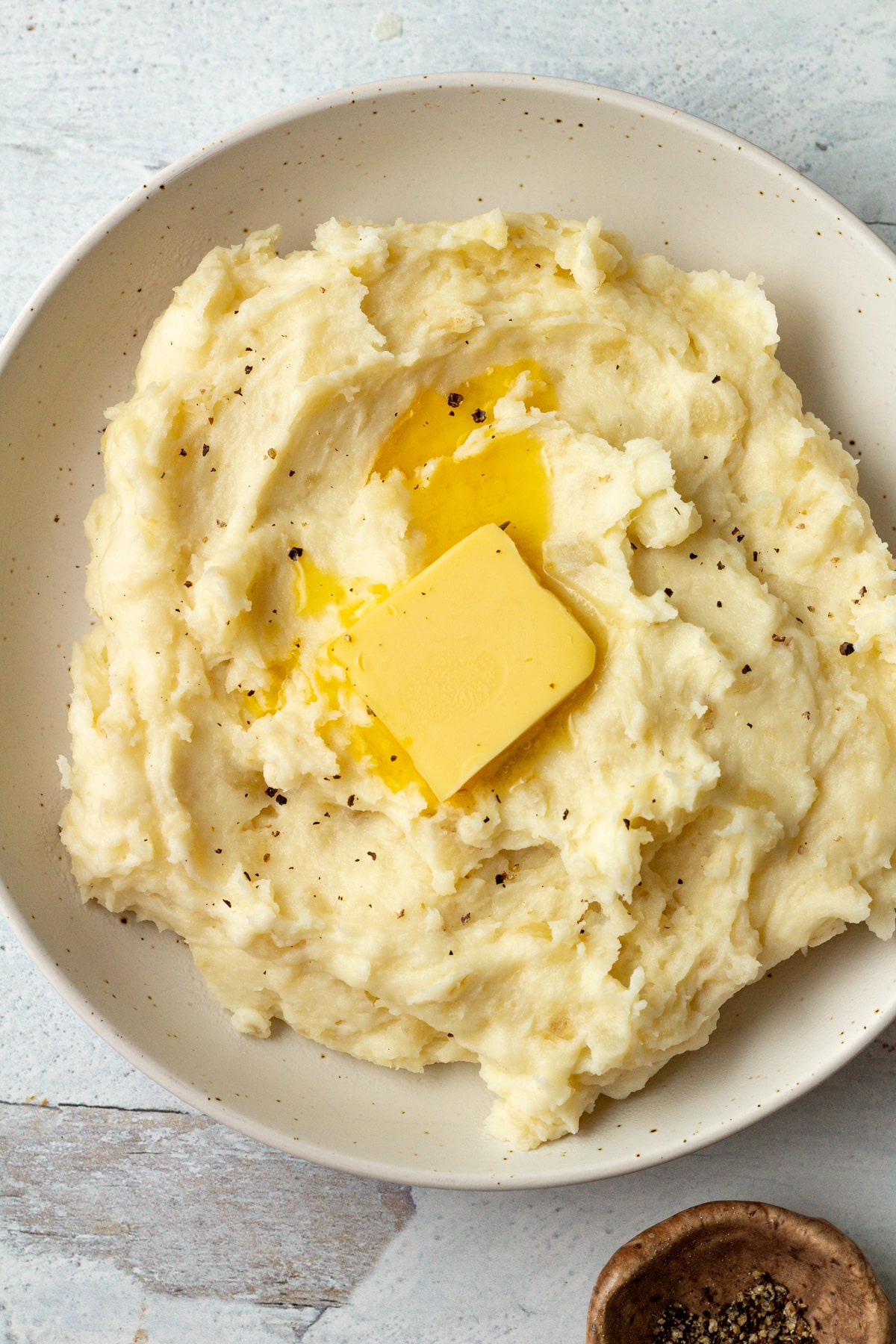 Mashed potatoes for two in bowl with pat of butter and black pepper on top.