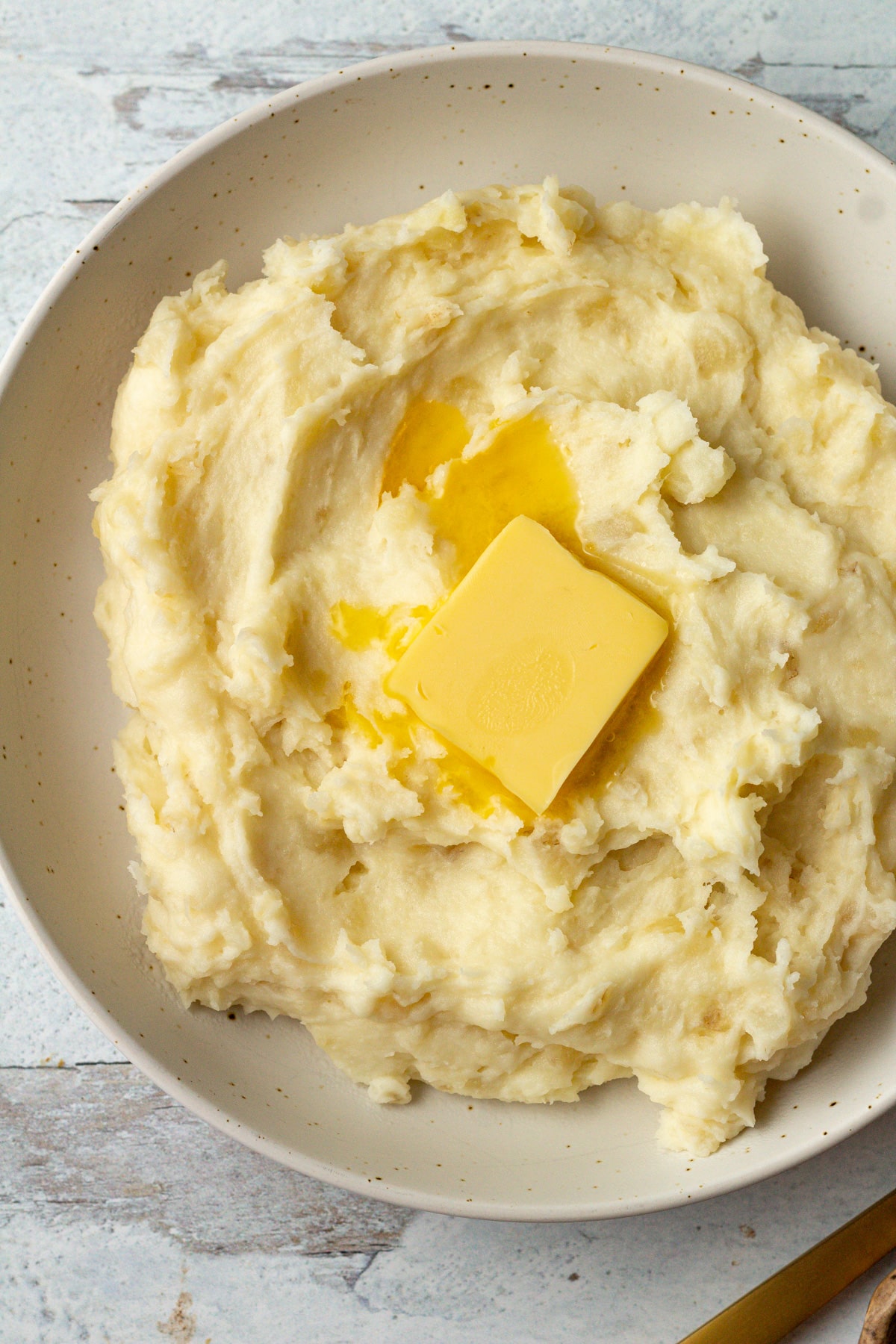 Mashed potatoes for two in serving bowl with butter on top.