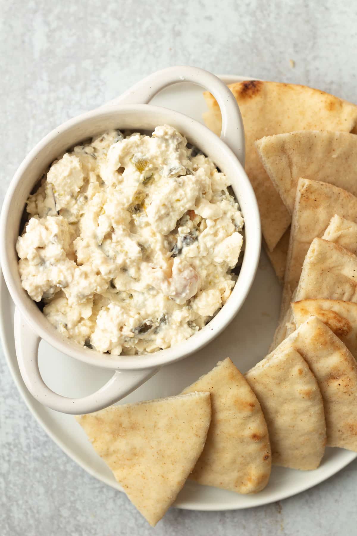 Spicy feta dip in bowl on plate with cut up pita.