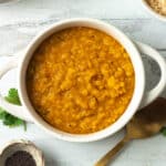 Small bowl of dal with spices and spoon on side.