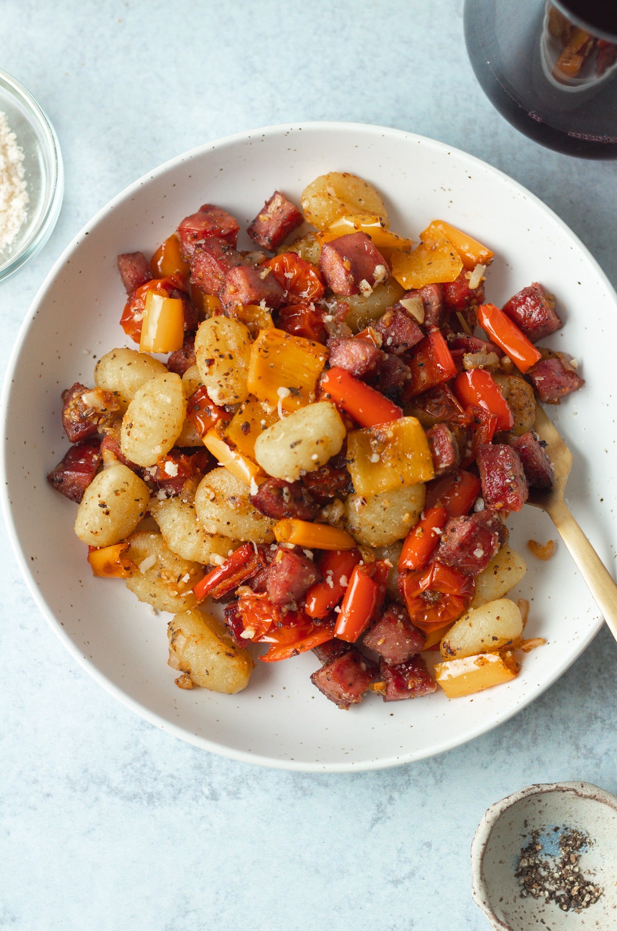 Bowl with sheet pan gnocchi and small garnish bowl of pepper on table.