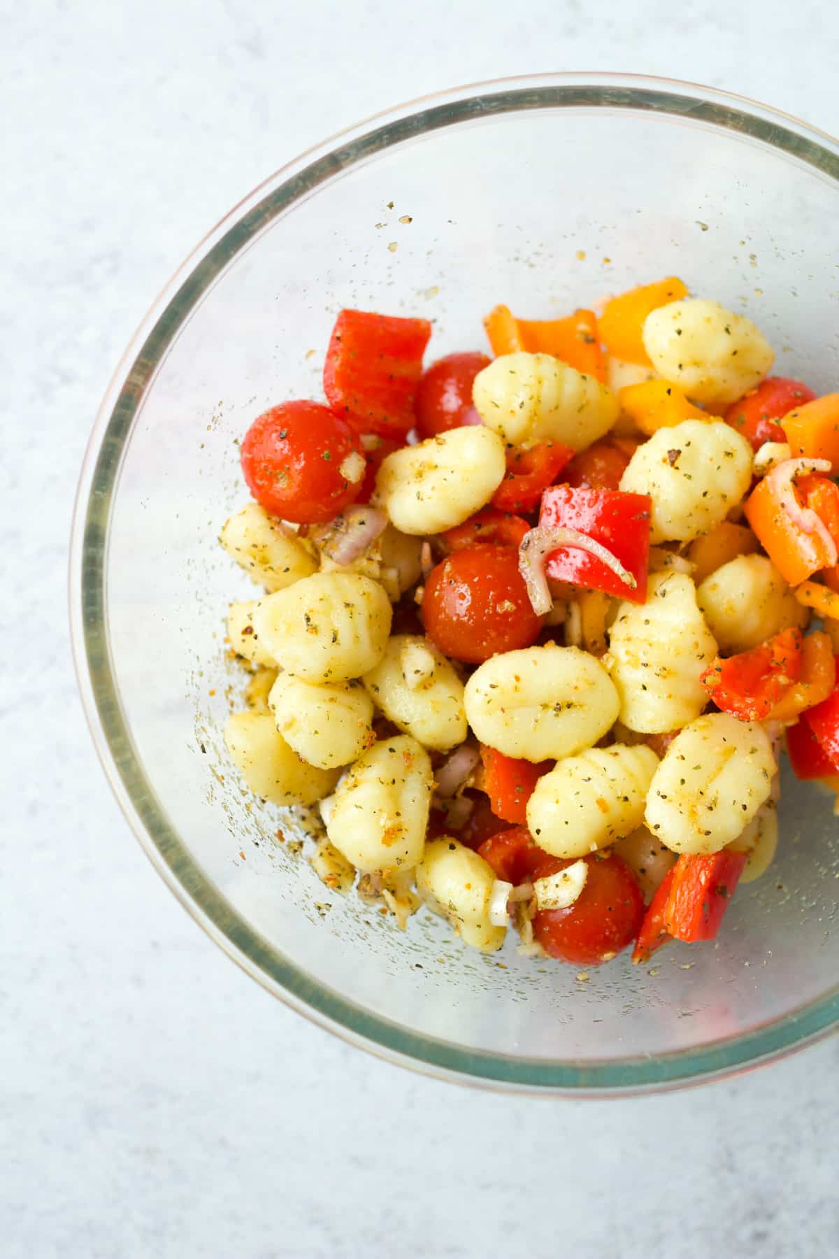 Gnocchi, peppers, tomatoes and onion in glass bowl.