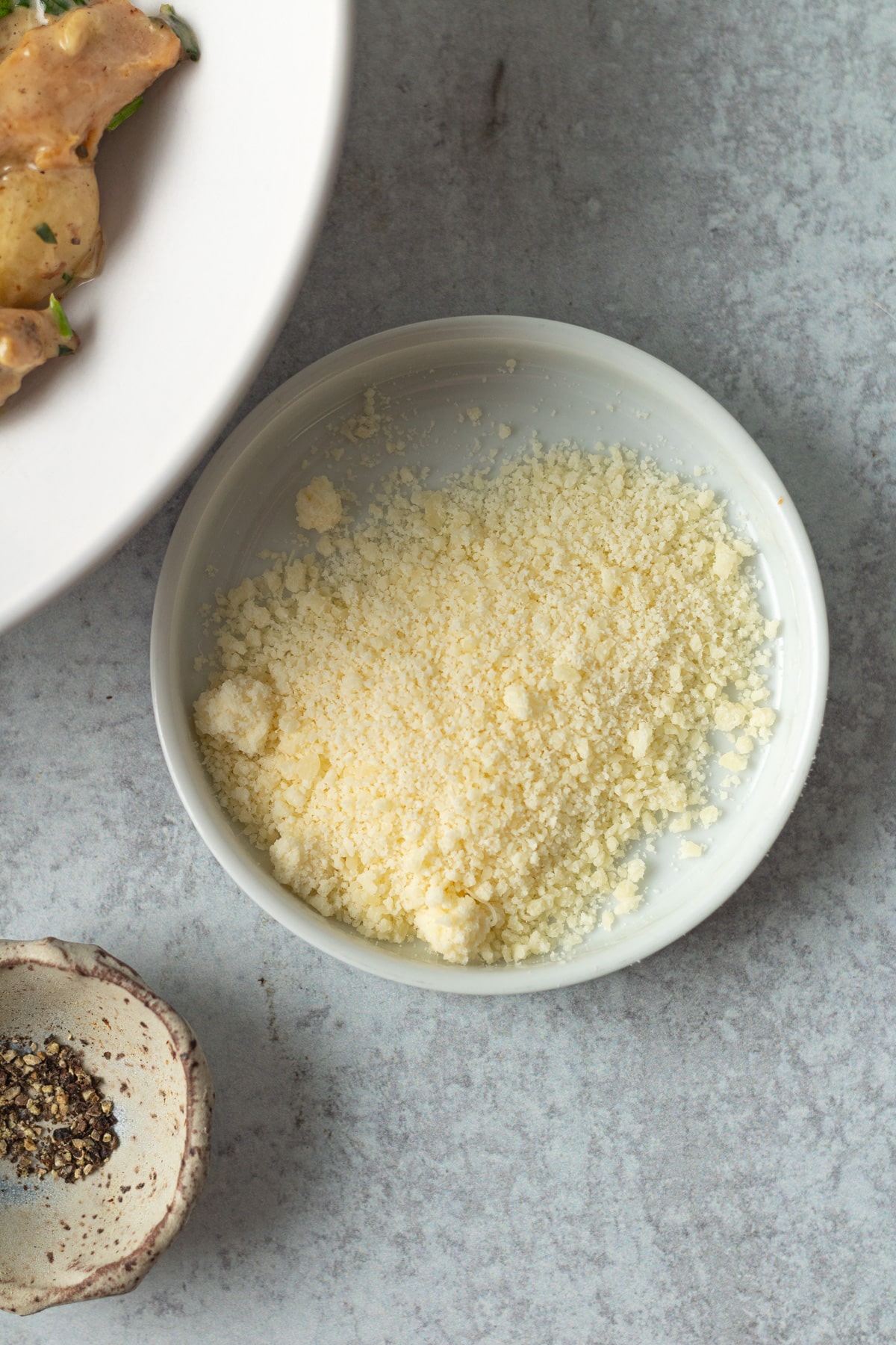 Small white dish of grated parmesan cheese.