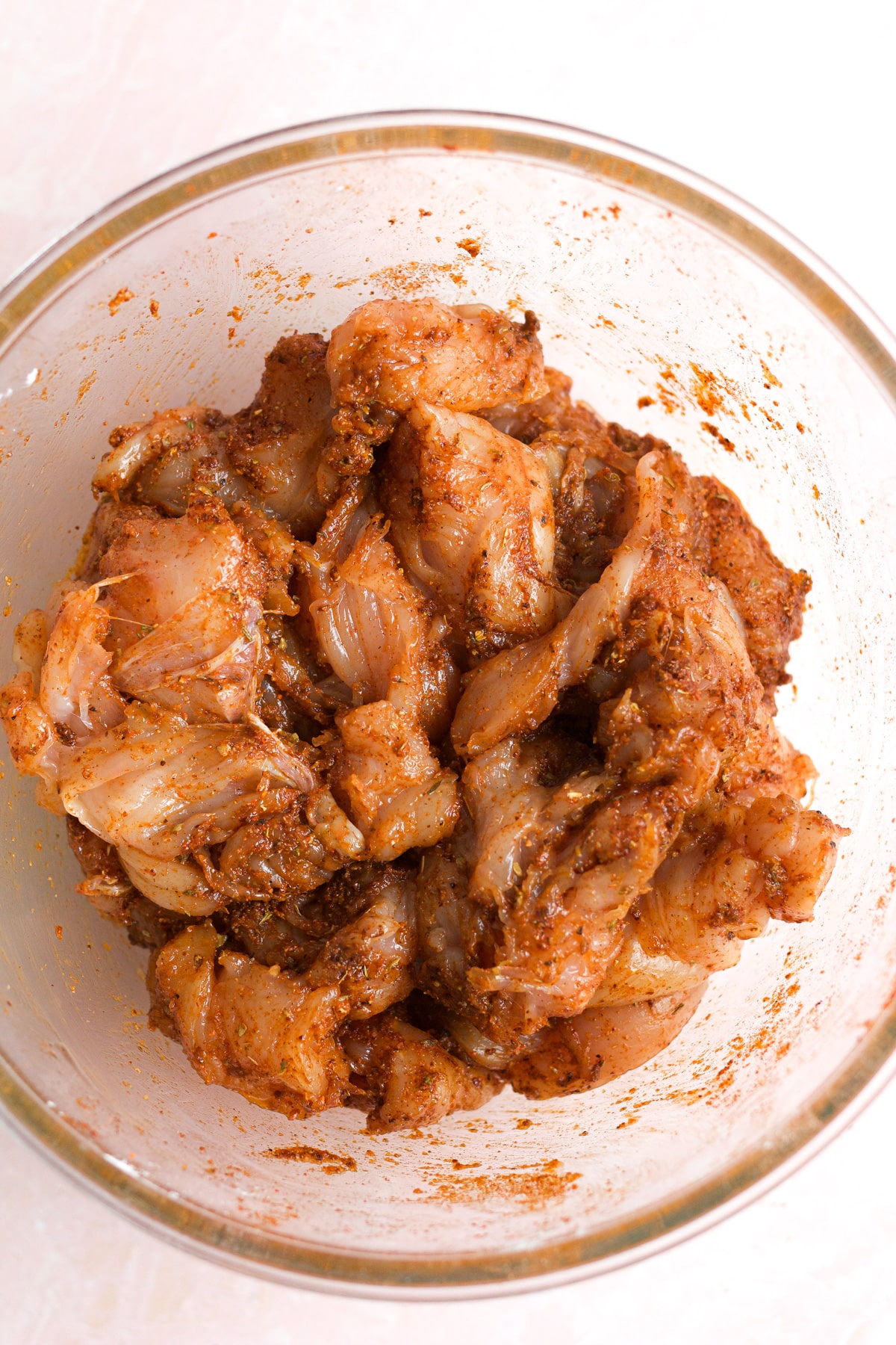 Raw chicken mixed with spices in glass bowl.