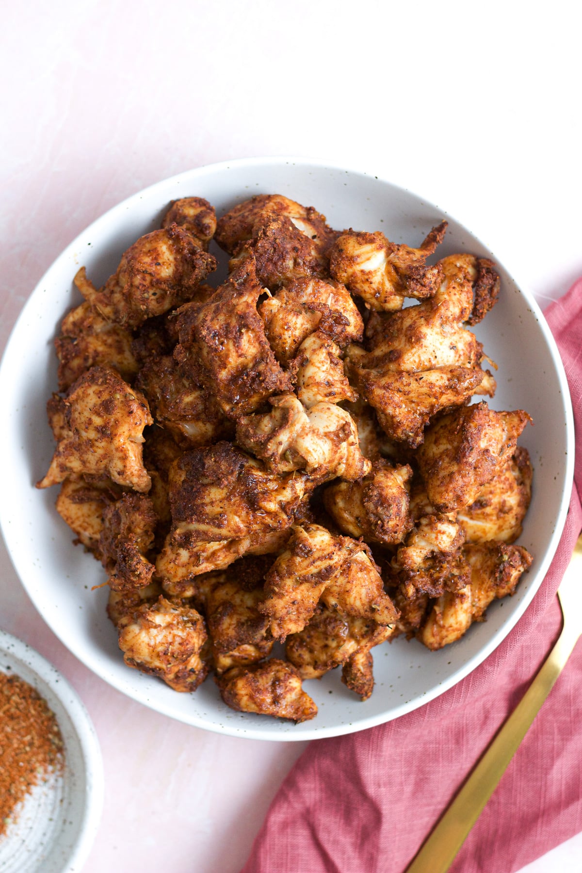 Air fryer chicken bites on white plate with spices and fork next to plate.